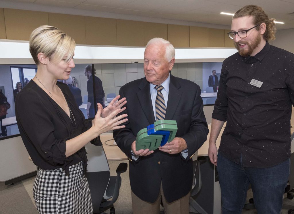 学生维吉尼亚·巴洛(左)和康纳·米尼利(右)向彼得·摩尔展示他们在创造空间中用3d打印机制作的加速器。