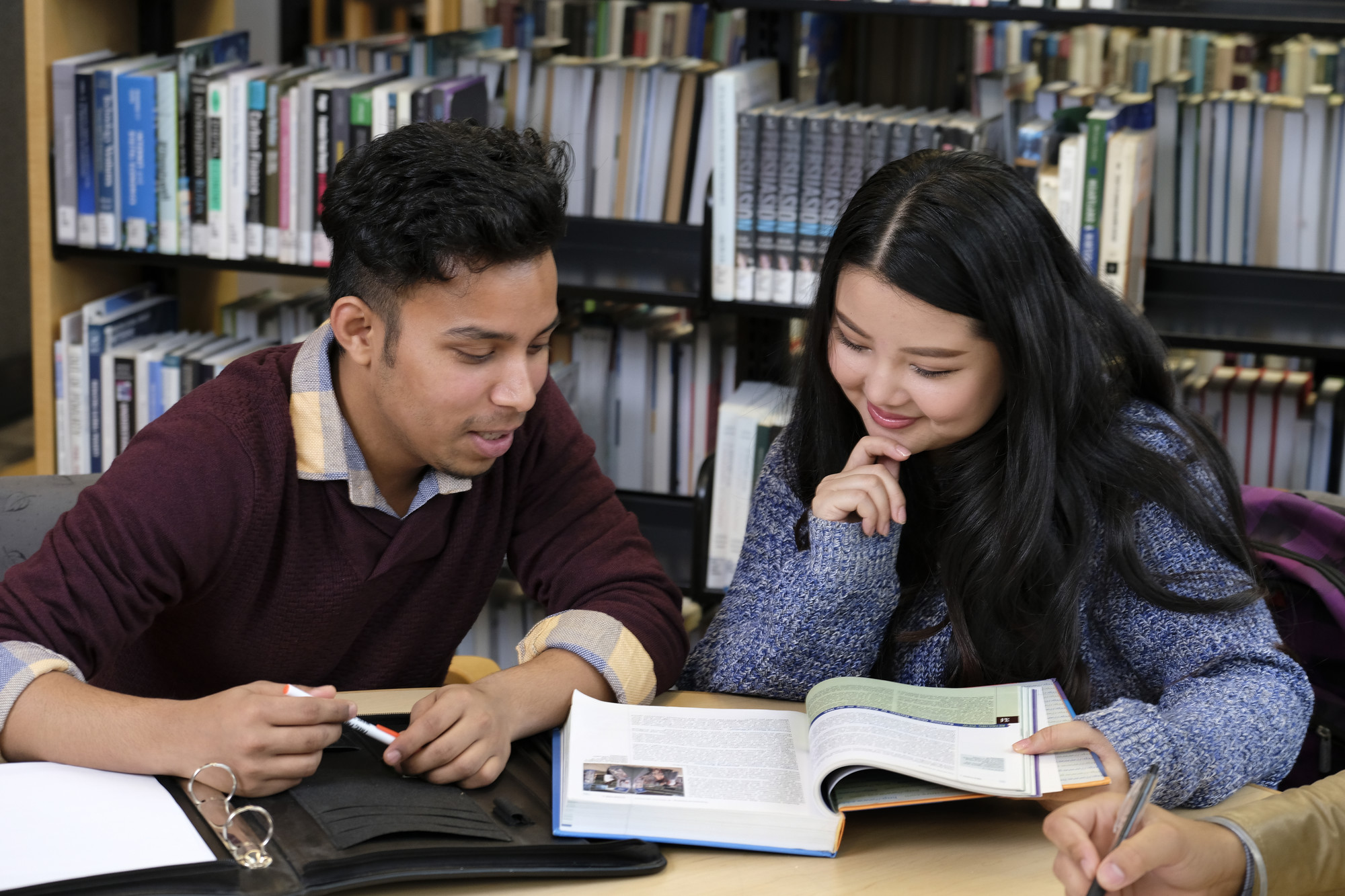 一个男学生和一个女学生坐在图书馆里读课本