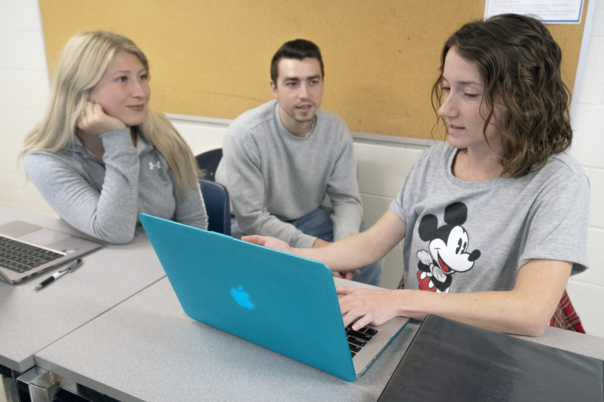 2名女学生和1名男学生坐在教室里用笔记本电脑工作