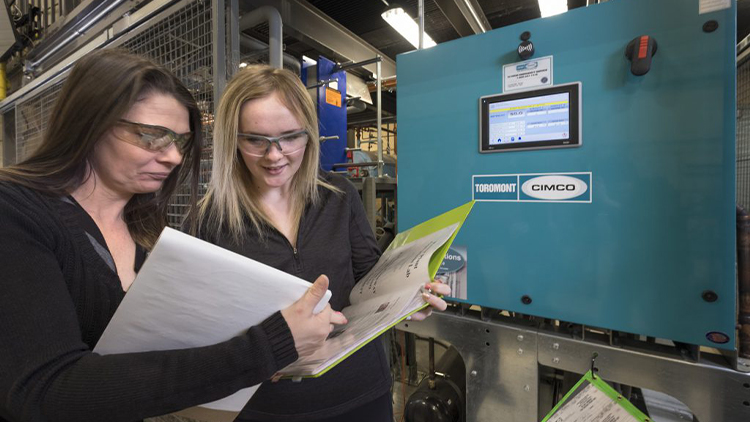 两名女学生戴着护目镜，在技术贸易实验室阅读活页夹