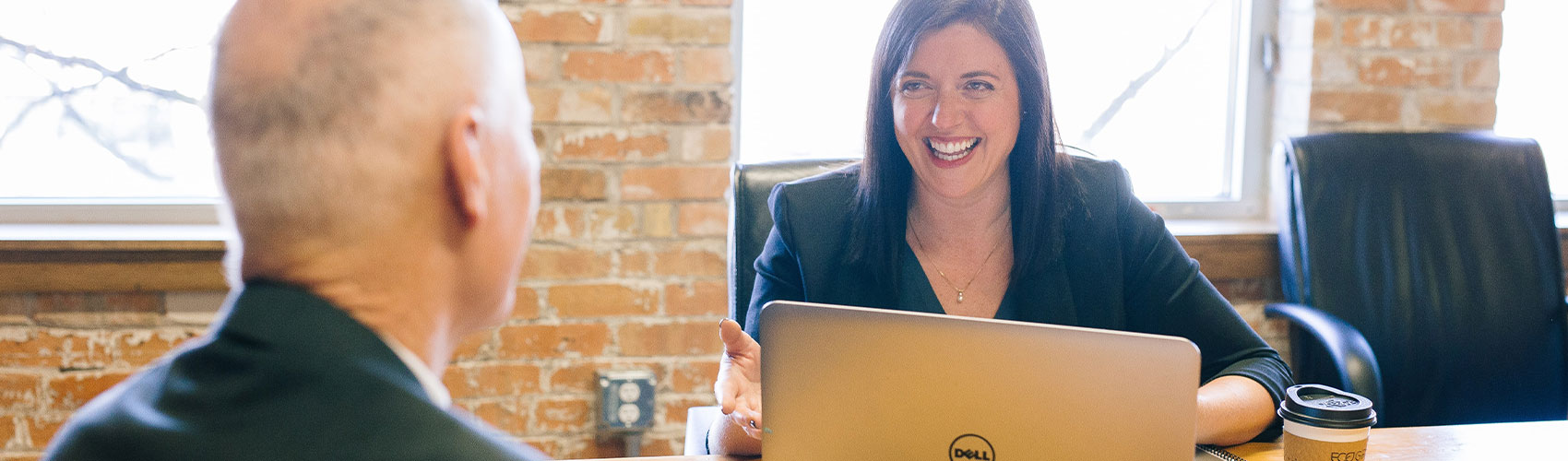 一位职业顾问坐在桌子旁，带笔记本电脑和咖啡杯，同时与雇主的联系微笑着聊天