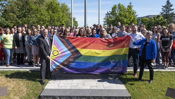 一群乔治亚人的雇员在Barrie Campus Cenotaph面前举行大型骄傲旗，在2022年骄傲月举行的旗帜上