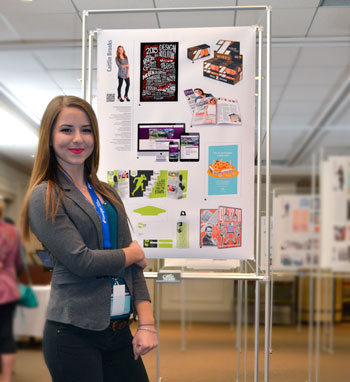 平面设计专业的学生站在展示她作品的海报板旁