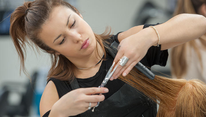 一个系着围裙的发型学生，用一把梳子和一把剪刀为客户修剪头发