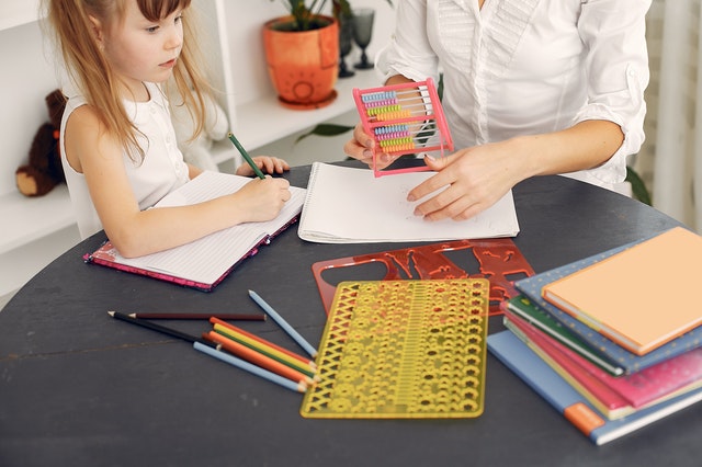 孩子和大人围坐在一张圆木桌旁，手里拿着笔记本、彩色铅笔和蜡笔
