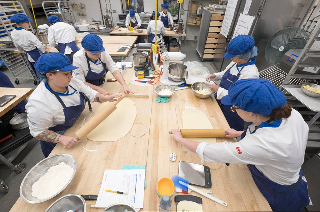 必赢彩票首页苹果官方版乔治亚学院烘焙和糕点艺术的学生穿着制服，围裙，发网和帽子在烘焙实验室制作糕点