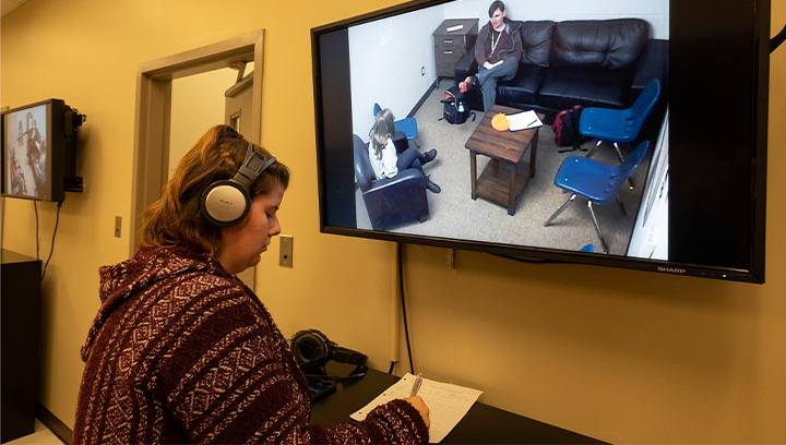 一名女学生戴着头戴式耳机，一边通过电视屏幕观看辅导课程，一边做笔记