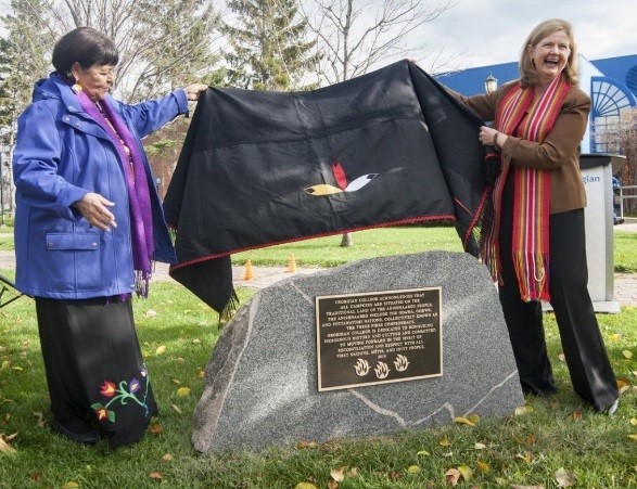 年长的Lorraine McRae和校长兼首席执行官MaryLynn West-Moynes在巴里校园外的一块石头上揭开了土地认可匾的面纱