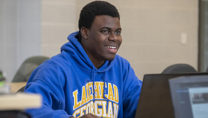 身穿lake head- georgia蓝色运动衫、面带微笑使用笔记本电脑的男生