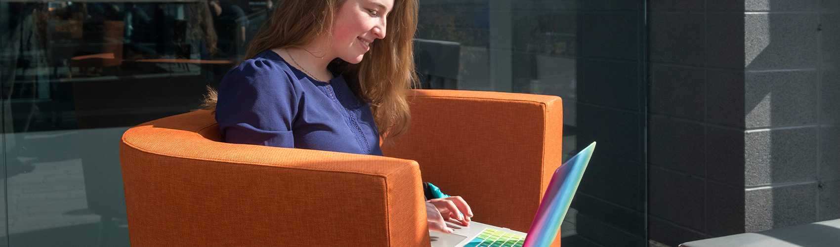 女学生用笔记本电脑坐在橙色的躺椅上