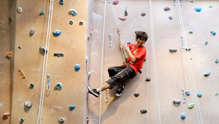 在巴利校区体育健身中心，一名男学生在攀岩墙上系上安全带