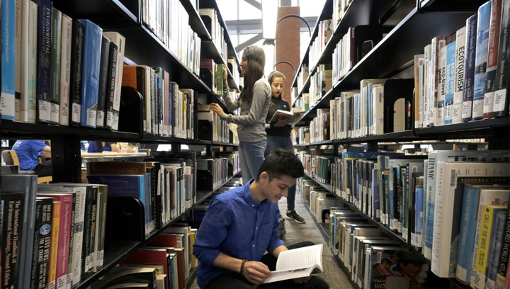三个学生站在图书馆的书架之间阅读
