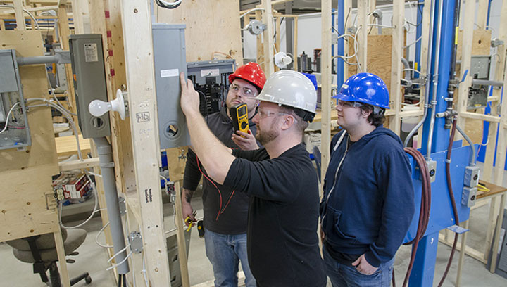 三个人戴着硬帽在电气面板上工作