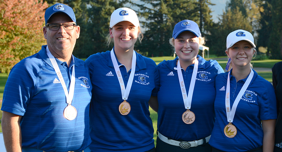 三名女子和一名男子身穿蓝色格鲁吉亚高尔夫球衫，脖子上挂着一枚奖牌，站在高尔夫球场上